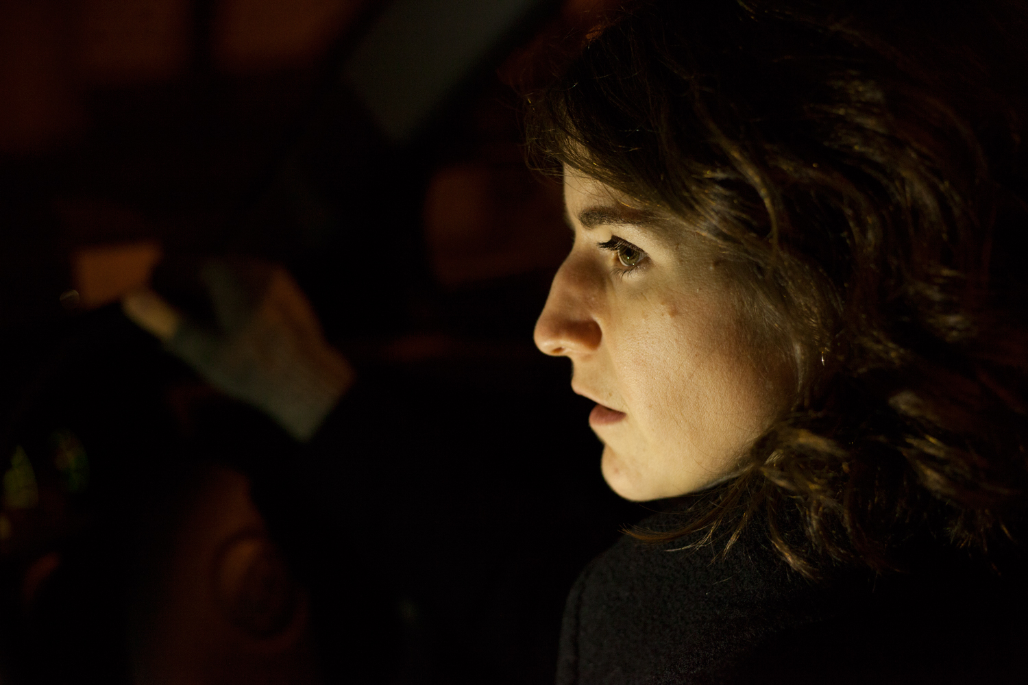 A woman places her hand on the steering wheel her face illuminated by an unseen light